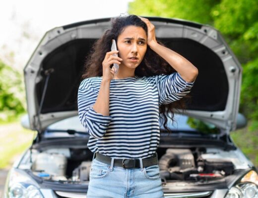 a young woman talking on the phone with a car’s open hood in the background