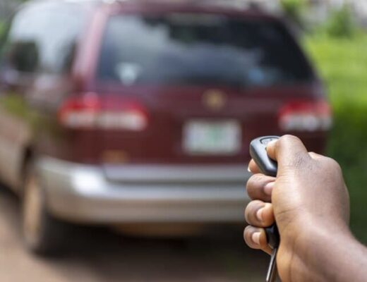 a hand using a car alarm remote control with a car in the background