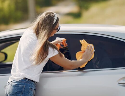 a woman wiping a car’s window with a dry yellow cloth